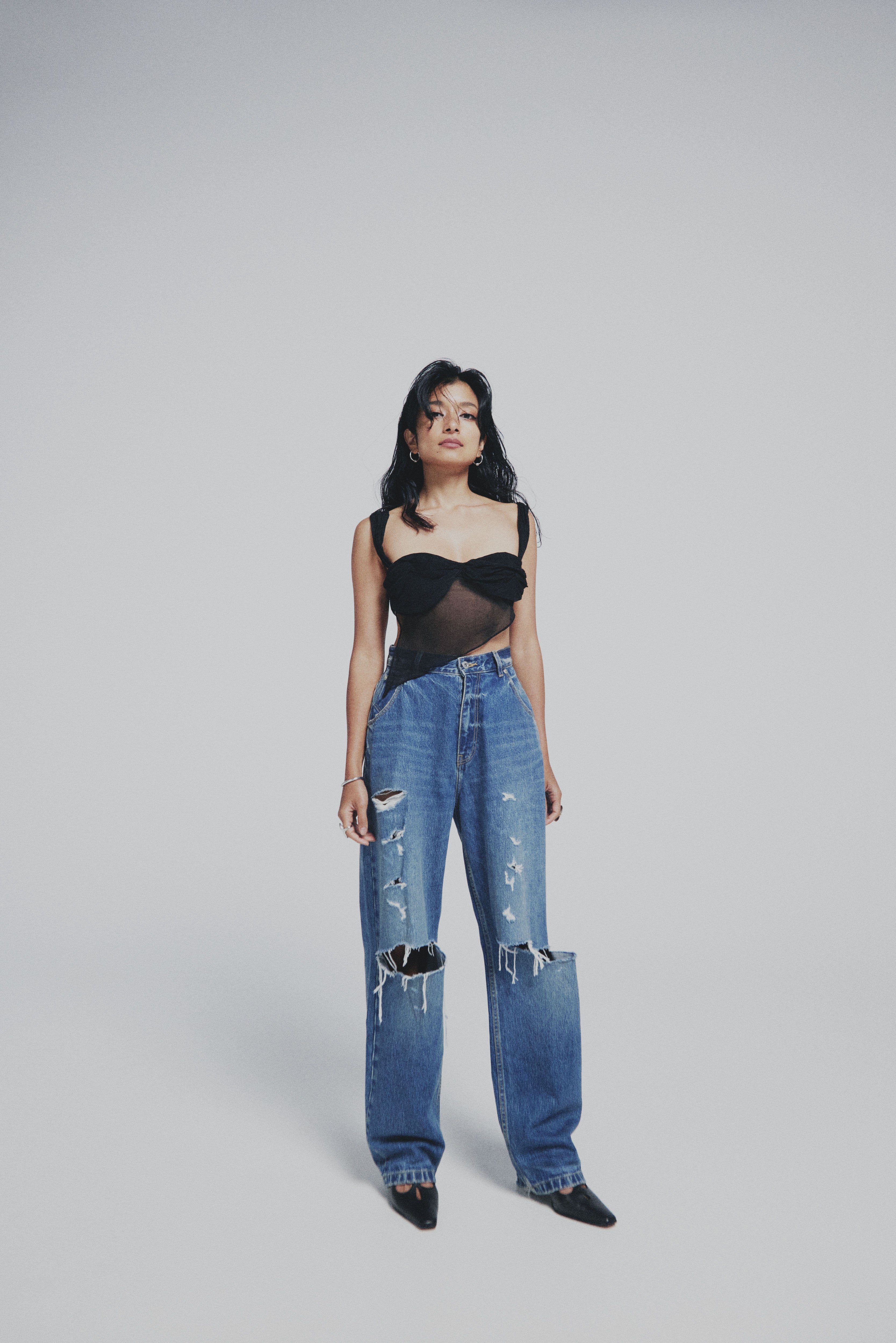 Woman wearing a black top and distressed blue jeans on a gray background