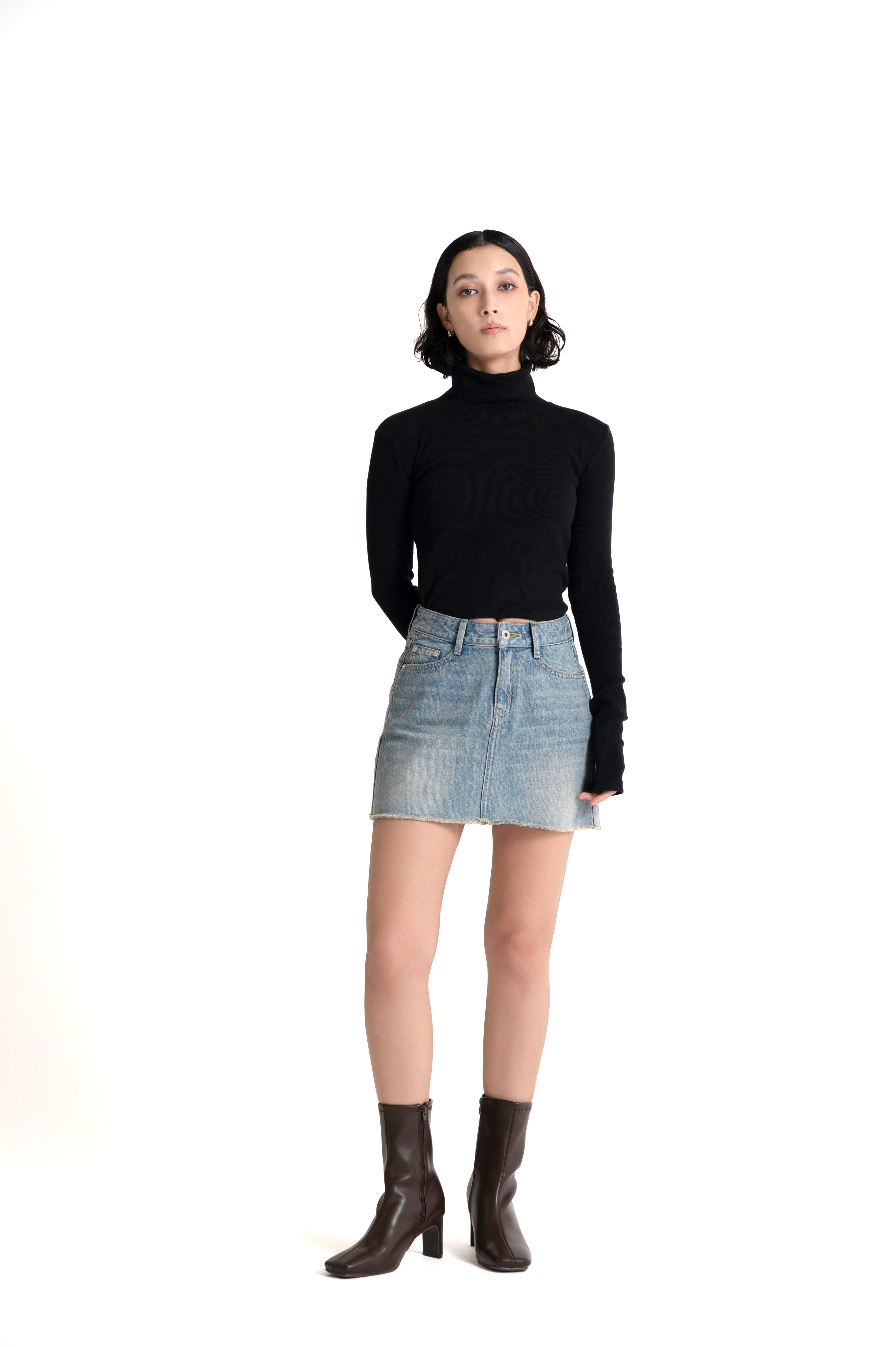Woman wearing a light indigo mini denim skirt, black turtleneck top and brown boots