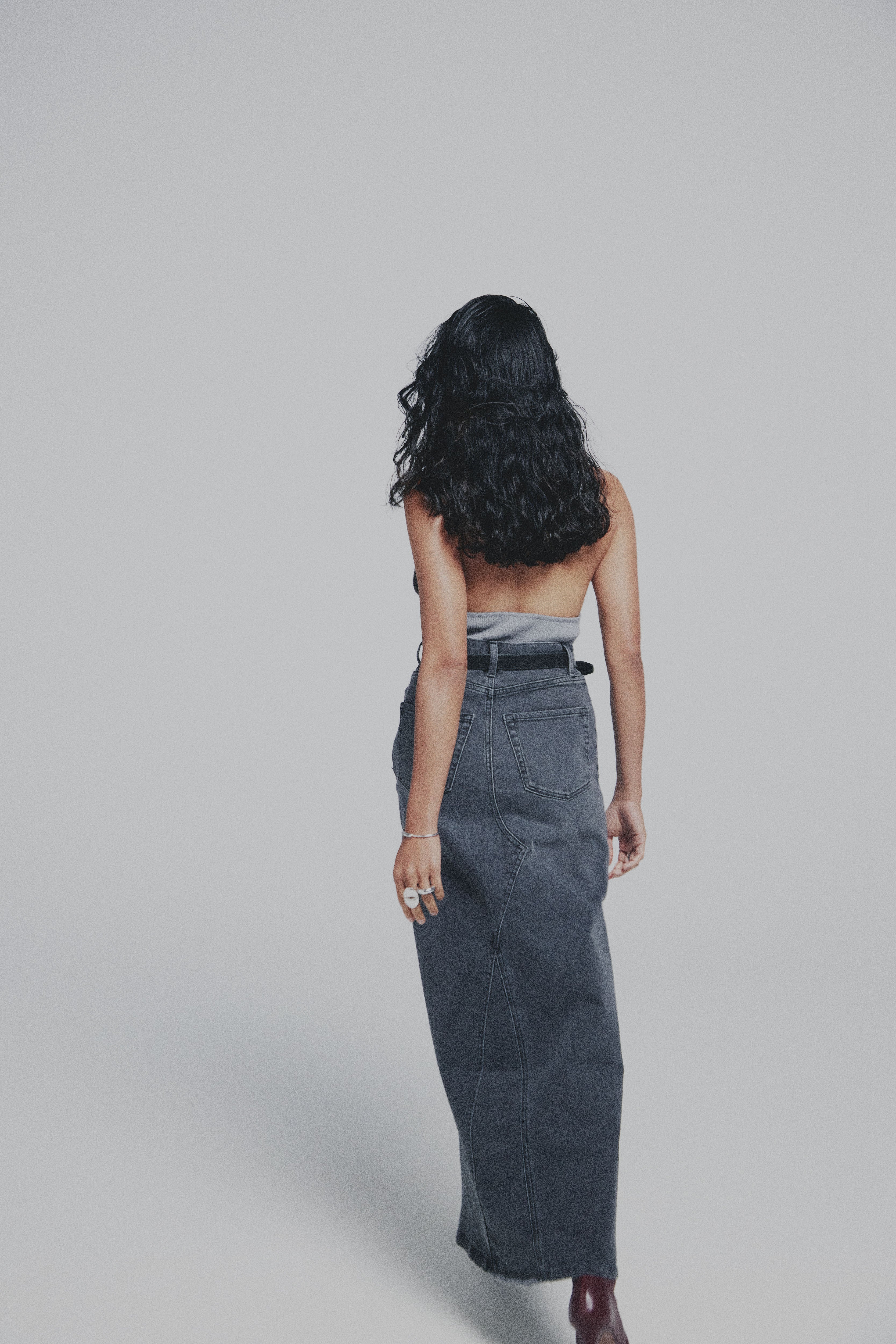 Woman wearing a long denim maxi skirt and strapless top on a plain background